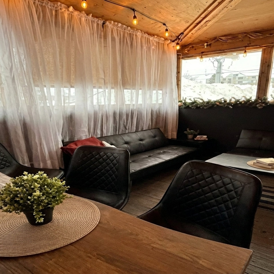 Cozy restaurant lounge with black leather seating, rustic wood tables, sheer curtains, warm string lights, and potted greenery.