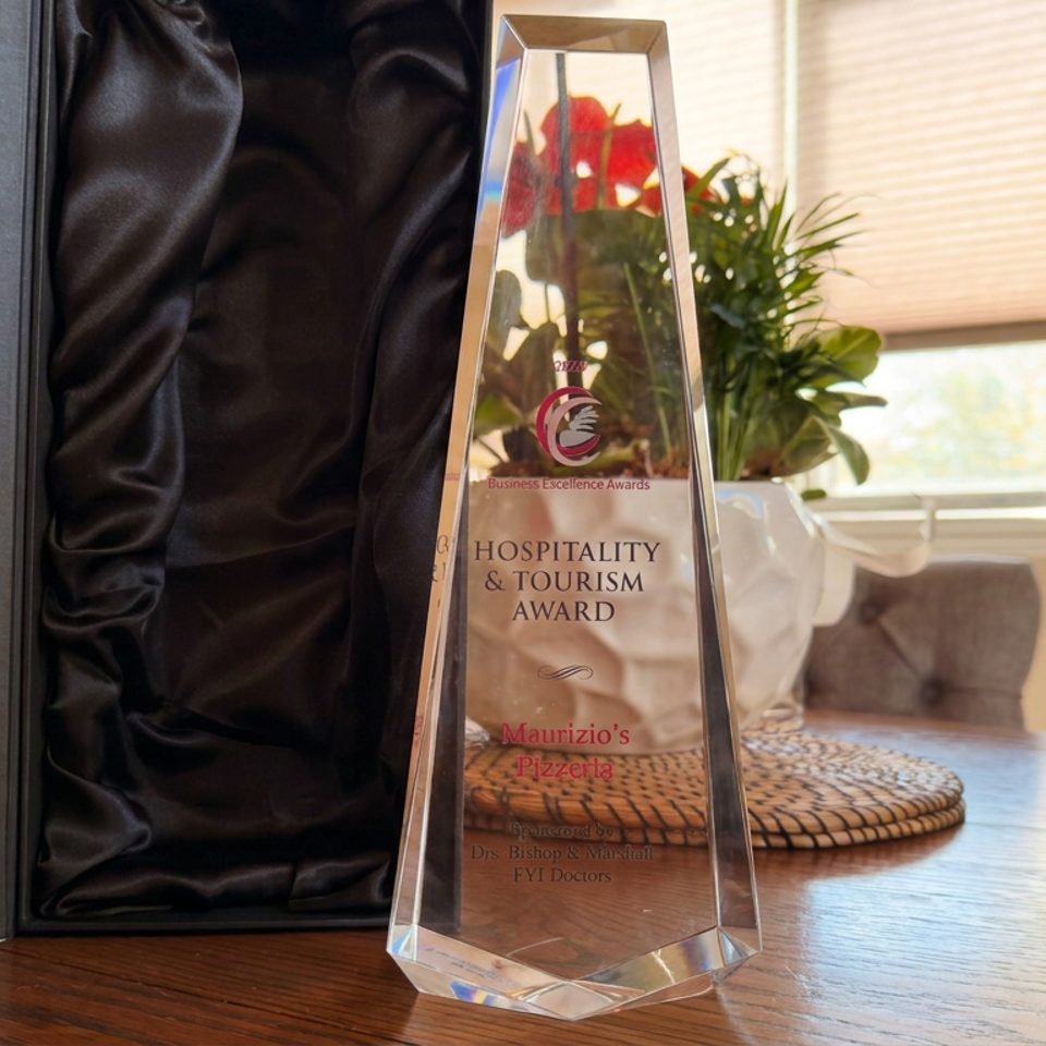 Hospitality and Tourism Award trophy for Maurizio’s Pizzeria displayed on a dining table beside a window and plant.