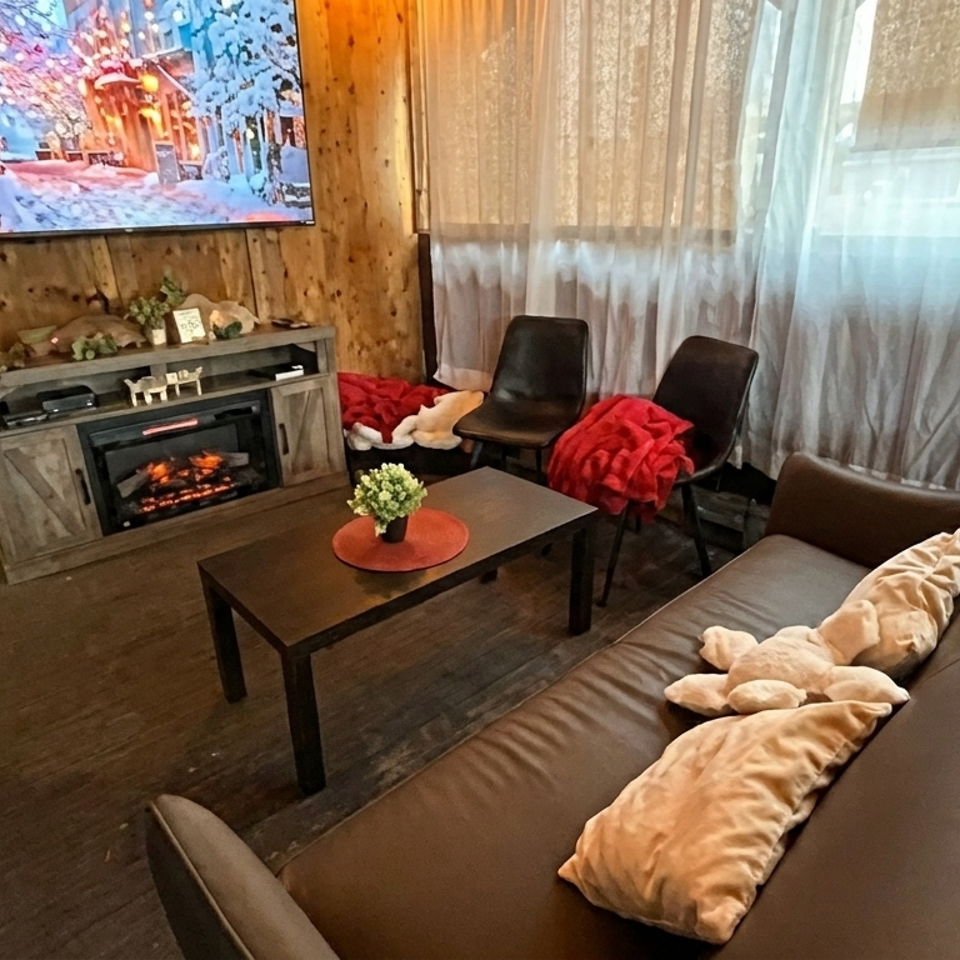Cozy wood-paneled lounge with leather sofa, armchairs, fireplace, coffee table, television, and warm blankets.